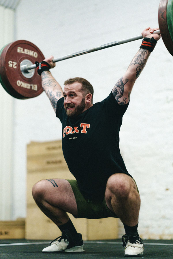 Man at a weightlifting gym holding weights above head.